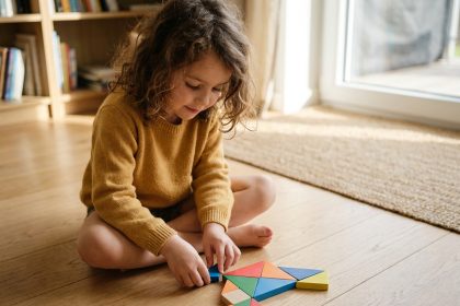 Petite fille apprenant les formes géométriques en jouant avec un tangram en bois coloré sur un parquet en chêne